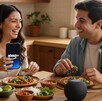 Pareja joven conversa con Alexa+ desde un teléfono celular mientras están en la cocina y comen comida mexicana