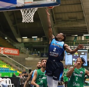 Un jugador de los Astros de Jalisco salta hacia la canasta para un enceste durante un partido contra los Caimanes en un estadio lleno de gente.