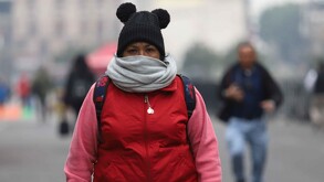 Se observa a una señora con chamarra, gorro y una bufanda; ella va caminando.