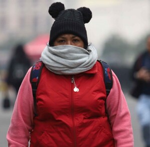Se observa a una señora con chamarra, gorro y una bufanda; ella va caminando.