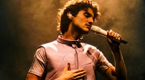 Cantante Humbe sosteniendo un micrófono y con la mano sobre el pecho durante un concierto con luz ambiental amarilla