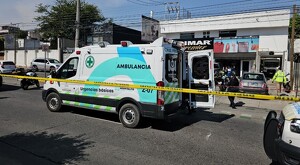 Ambulancia de la Cruz Verde con una puerta abierta delante de una tintorería con patrullas y policías de Zapopan alrededor. Una cinta policiaca en primer plano