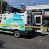 Ambulancia de la Cruz Verde con una puerta abierta delante de una tintorería con patrullas y policías de Zapopan alrededor. Una cinta policiaca en primer plano