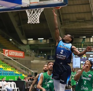 Un jugador de los Astros de Jalisco salta hacia la canasta para un enceste durante un partido contra los Caimanes en un estadio lleno de gente.
