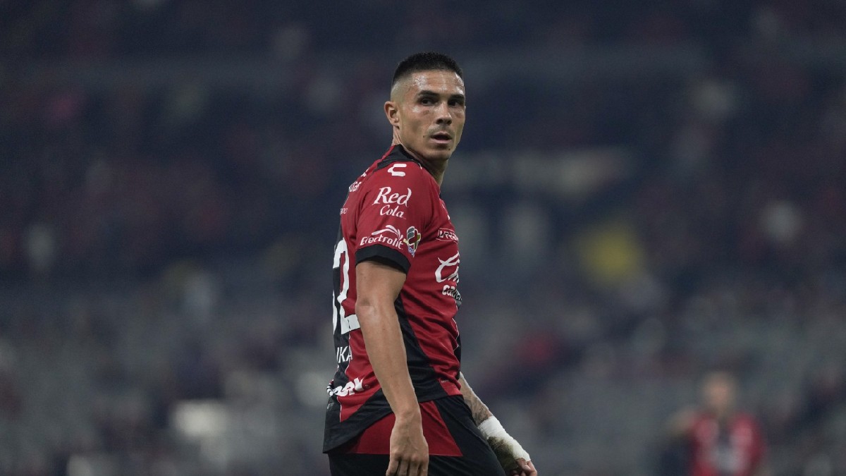 Un jugador del Atlas FC mira hacia atrás sobre su hombro en un estadio nocturno, vistiendo su camiseta rojinegra con patrocinios visibles.