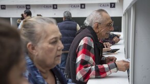 Se observa a unos adultos mayores haciendo fila frente a una ventanilla.