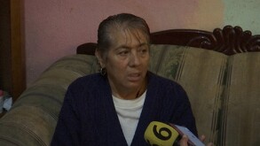 Se observa a una mujer de la tercera edad con cabello corto, con fleco, y con blusa blanca y suéter azul.