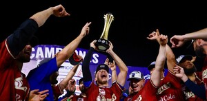Jugadores de los Charros de Jalisco celebran con júbilo en el campo, mientras uno de ellos levanta el trofeo de campeones hacia el cielo nocturno.