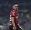 Un jugador del Atlas FC mira hacia atrás sobre su hombro en un estadio nocturno, vistiendo su camiseta rojinegra con patrocinios visibles.