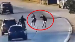 Dos sujetos enmarcados en un cirulo rojo apuntando a un motociclista en medio de una autopista con autos circulando alrededor