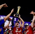 Jugadores de los Charros de Jalisco celebran con júbilo en el campo, mientras uno de ellos levanta el trofeo de campeones hacia el cielo nocturno.