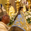 Padre sosteniendo una figura de la Virgen de San Juan de los Lagos dentro de la Basílica con adornos y personas alrededor