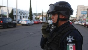 Oficial de la Guardia Civil en Michoacán hablando por un radio con casas, autos y edificios desenfocados de fondo