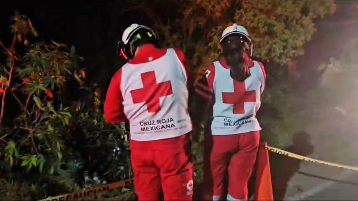 Dos paramédicos de la Cruz Roja delante de una barraca a un costado de la carretera acordonada por una cinta policiaca y conos