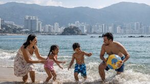 Familia disfrutando de las vacaciones de semana santa y jugando frente al mar de Acapulco con una pelota en un día soleado.