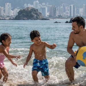 Familia disfrutando de las vacaciones de semana santa y jugando frente al mar de Acapulco con una pelota en un día soleado.