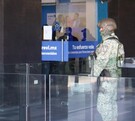 Se observa a un hombre con uniforme de militar y con el rostro cubierto, afuera de un edificio con cartelones azules.
