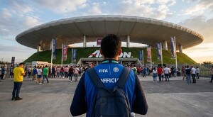 Voluntario con chaleco de la FIFA visto de espaldas mientras está de pie frente al Estadio Akron en Guadalajara con una multitud de personas alrededor