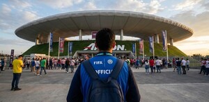 Voluntario con chaleco de la FIFA visto de espaldas mientras está de pie frente al Estadio Akron en Guadalajara con una multitud de personas alrededor