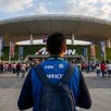 Voluntario con chaleco de la FIFA visto de espaldas mientras está de pie frente al Estadio Akron en Guadalajara con una multitud de personas alrededor