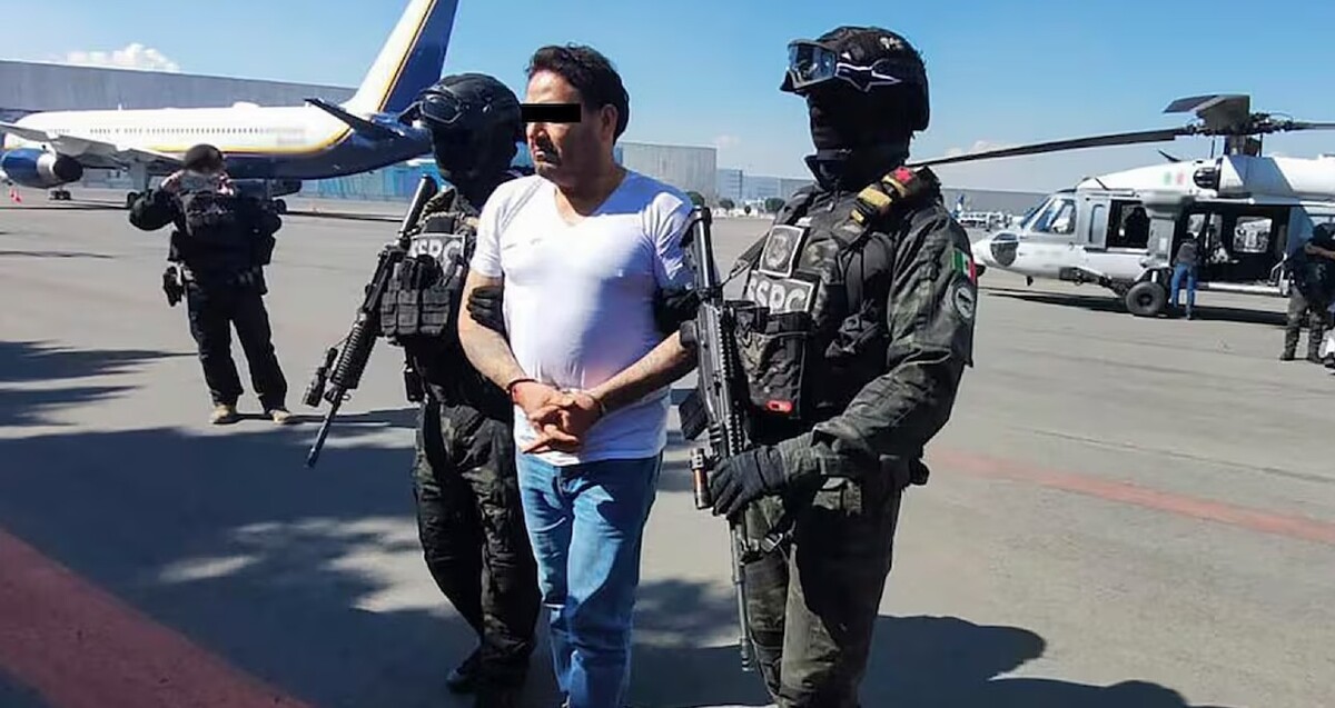 César Alejandro, alias El Bótox siendo sujetado por dos oficiales de la SSPC con un avión y un helicóptero detrás y un camarógrafo a la izquierda