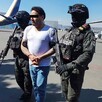César Alejandro, alias El Bótox siendo sujetado por dos oficiales de la SSPC con un avión y un helicóptero detrás y un camarógrafo a la izquierda