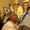 Padre sosteniendo una figura de la Virgen de San Juan de los Lagos dentro de la Basílica con adornos y personas alrededor