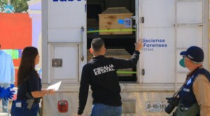 Dos miembros de la Fiscalía y un trabajador del Gobierno de Jalisco frente a un camión del IJCF con féretros de madera dentro