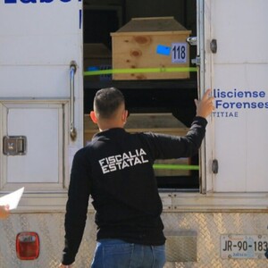 Dos miembros de la Fiscalía y un trabajador del Gobierno de Jalisco frente a un camión del IJCF con féretros de madera dentro