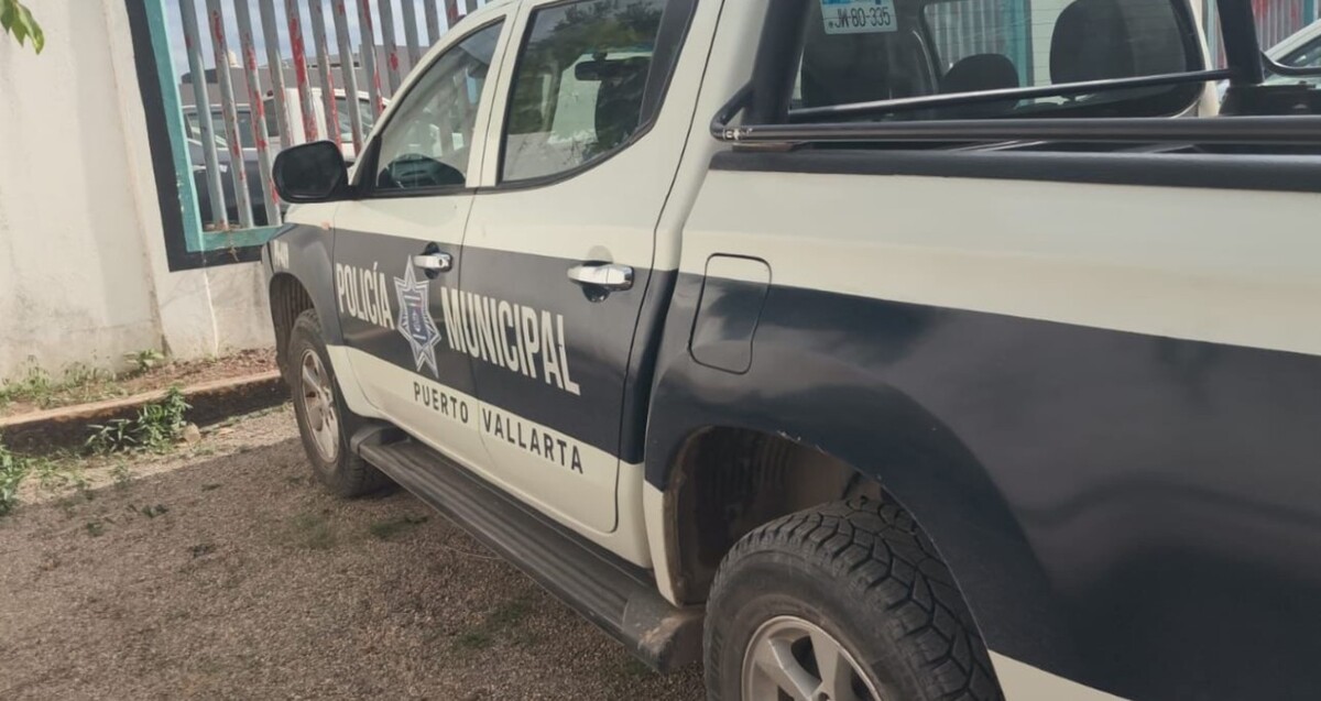 Vista del costado de una Patrulla de la Policía Municipal de Puerto Vallarta estacionada al exterior de un edificio con barda blanca