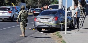 Militar del Ejército al lado de un Nissan Versa color gris acordonado por una cinta policiaca con personas alrededor y autos transitando al lado