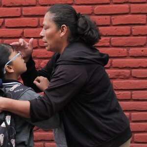 Una mujer da la bendición a su hija antes de dejarla en la escuela.