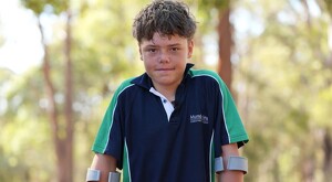 Niño identificado como Austin Appelbee viendo de frente mientras posa para una foto con árboles y plantes desenfocadas en el fondo