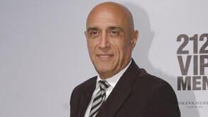 Se observa a un hombre sin cabello y vistiendo un traje color gris.