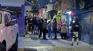 Multitud de personas reunidas al exterior de una tienda de abarrotes con elementos de la Guardia Nacional resguardando un área acordonada entre casas y autos