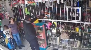 Asaltante recibiendo dinero de una cajera al interior de una papelería con una madre y su hija observando a la izquierda