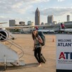 Mujer con mochila y maleta acercándose a la escalera de un avión en el aeropuerto de Atlanta con aviones estacionados detrás