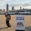 Mujer con mochila y maleta acercándose a la escalera de un avión en el aeropuerto de Atlanta con aviones estacionados detrás