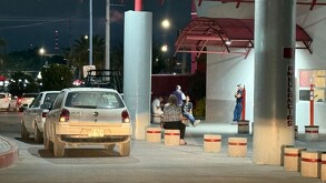Se observa una camioneta blanca estacionada y al fondo unas personas sentadas.