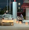 Se observa una camioneta blanca estacionada y al fondo unas personas sentadas.