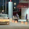 Se observa una camioneta blanca estacionada y al fondo unas personas sentadas.