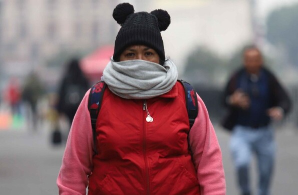 Se observa a una señora con chamarra, gorro y una bufanda; ella va caminando.