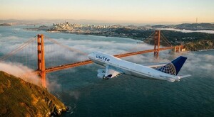 Avión de la aerolínea United Airlines sobrevolando el puente de San Francisco con vistas del mar y la ciudad al fondo cubiertas por un poco de nubes
