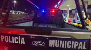 Vista de la parte trasera de una patrulla de la Policía Municipal de Zapopan con las sirenas encendidas al exterior de dos estaciones de una gasolinera