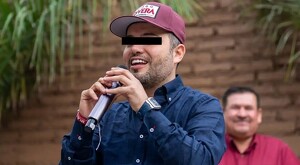 Diego Rivera Navarro sonriendo mientras sostiene un micrófono con ambas manos y con los ojos censurados por un rectángulo negro