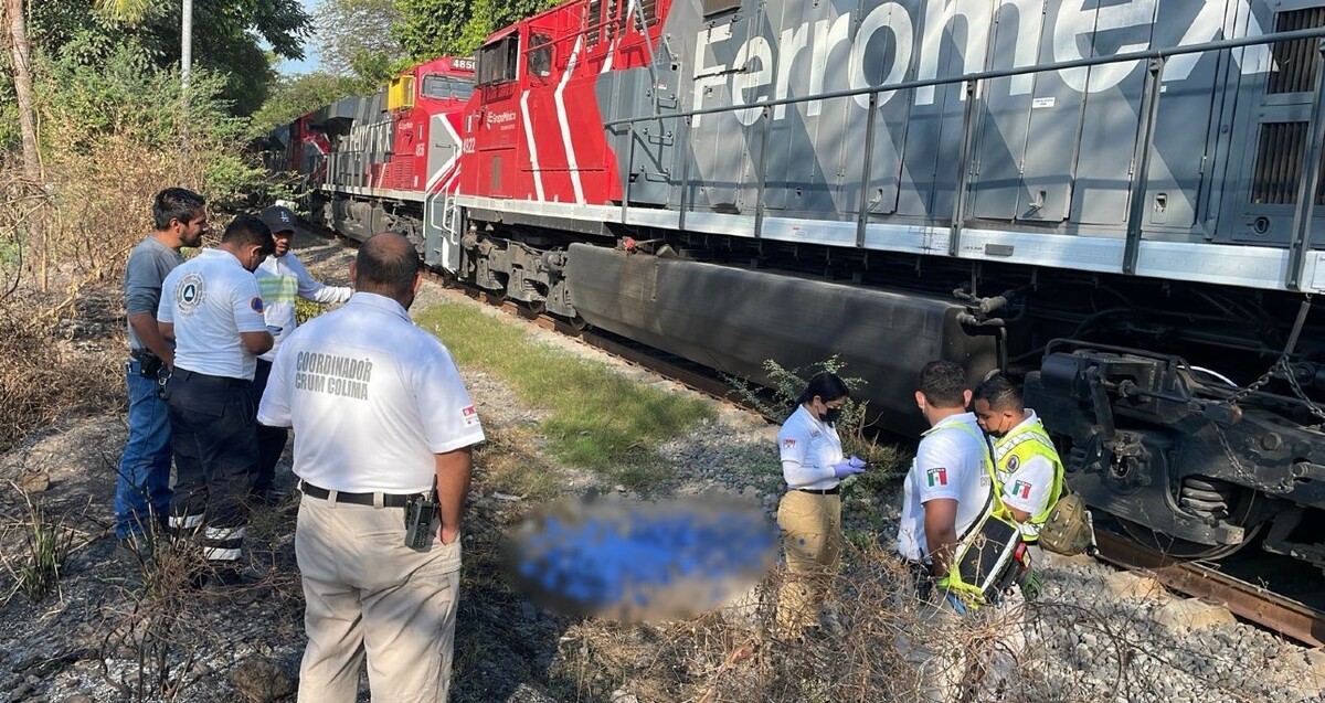 Elementos de Protección Civil de Colima al lado de un tren de la empresa Ferromex y con el cuerpo de un hombre cubierto por una manta azul en el suelo
