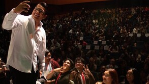 Se observa a un joven vistiendo camisa blanca y con muchas personas atrás.