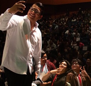 Se observa a un joven vistiendo camisa blanca y con muchas personas atrás.