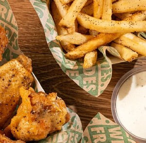 Se obseva un plato de alitas, unas papas fritas y un aderezo blanco.