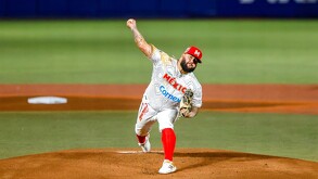 Un lanzador de los Charros de Jalisco, con uniforme de México y gorra roja, realiza un lanzamiento desde la loma durante un partido nocturno.